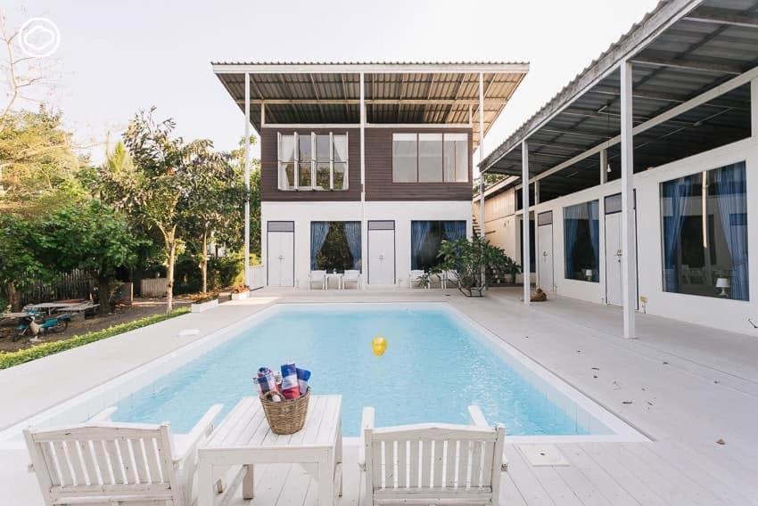 a swimming pool with two chairs and a house at Arthit -Tara Lodge in Prachin Buri