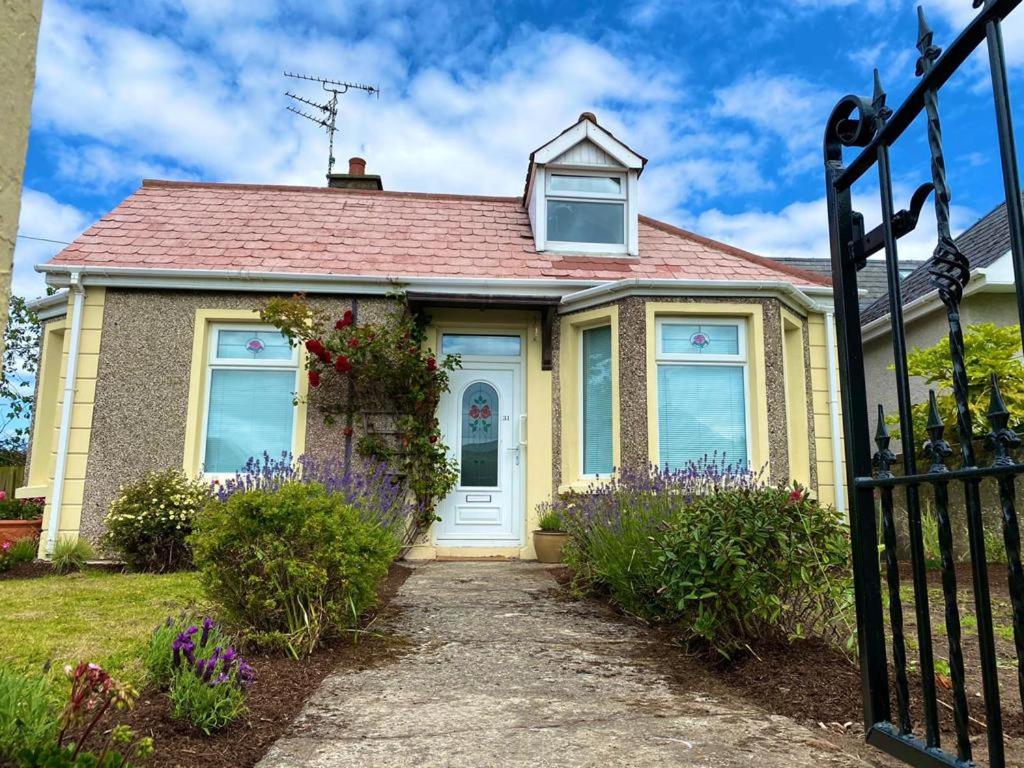 een geel huis met een witte deur en bloemen bij Rose Cottage: Delightful 4 bedroom detached home in Portrush