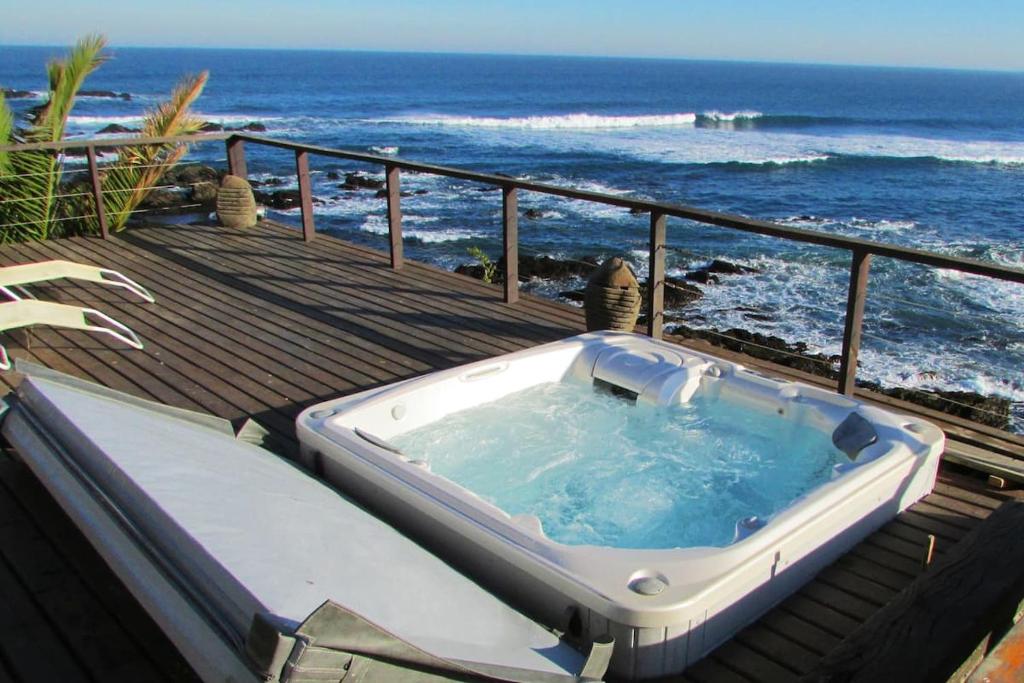 a jacuzzi tub sitting on a deck next to the ocean at Increíble casa primera línea frente a ola Infiernillo in Pichilemu