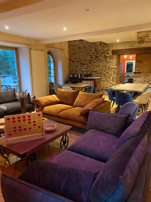 a living room with couches and tables and a stone wall at Ancien Moulin rénové à neuf pour 20 personnes sur les rives du Trieux in Plésidy
