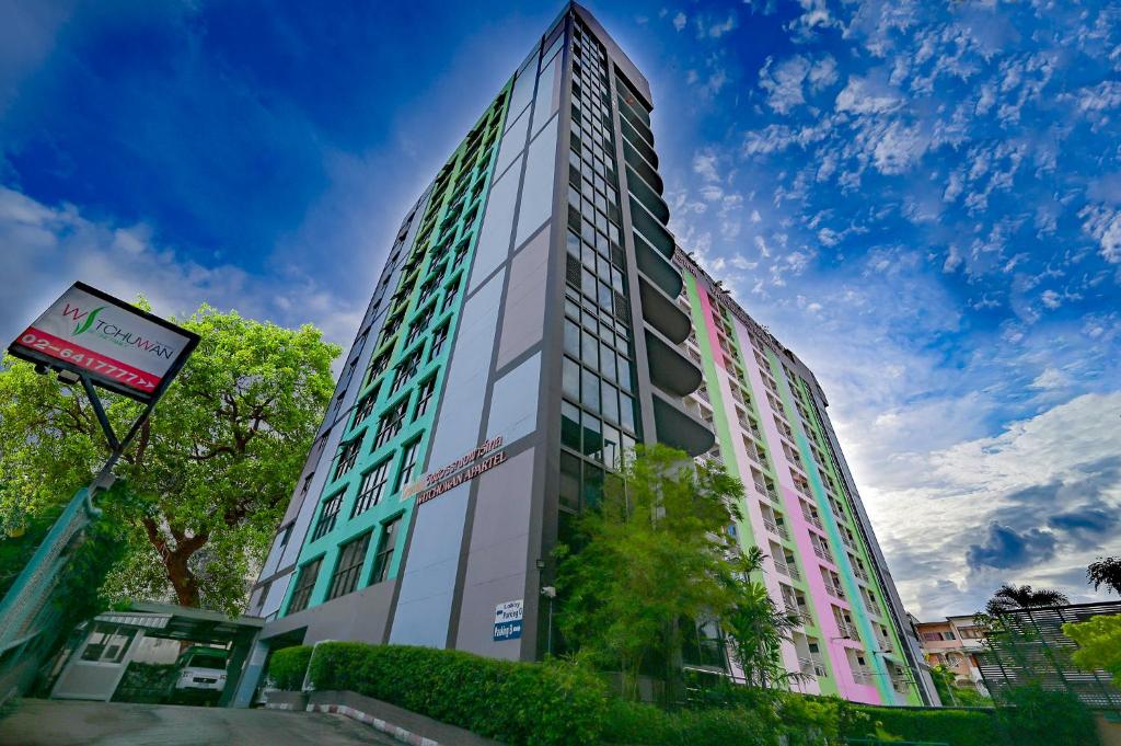 een hoog gebouw met groene ramen aan een stadsstraat bij Witchuwan Apartel in Bangkok