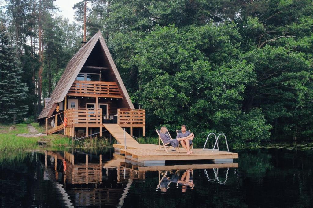 a person sitting in a chair on a dock in front of a house at Saarjärve Puhkemaja Saunamaja in Viira