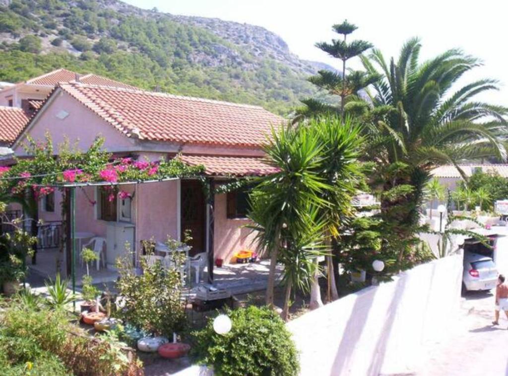 a house with palm trees in front of a mountain at "Patra's" Apartments Patra in Poseidónion