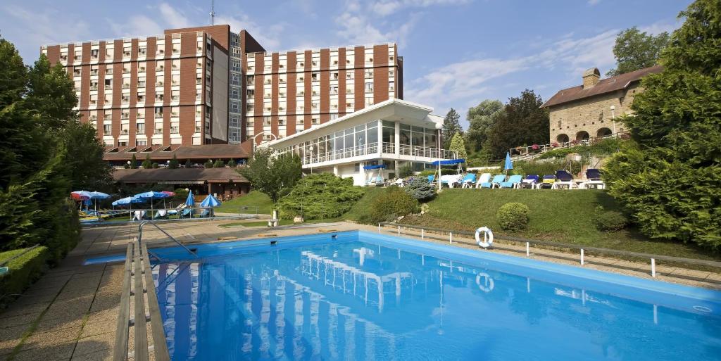 a large building with a pool and lawn chairs in front of it at Ensana Thermal Aqua in Hévíz