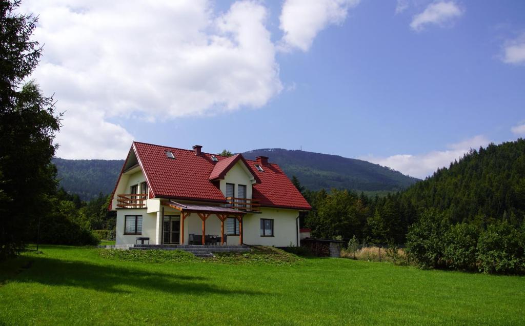 une maison avec un toit rouge sur un champ vert dans l'établissement Dom pod Skrzycznem, à Lipowa