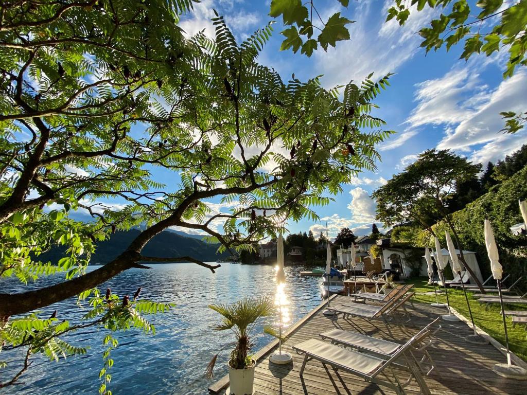 a view of a lake with chairs and trees at Hotel Nikolasch in Millstatt