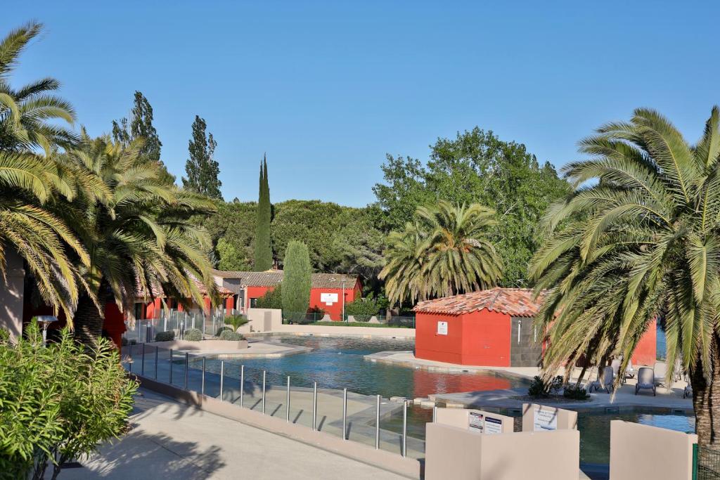 ein Resort mit einem Pool und Palmen in der Unterkunft SOWELL HOTELS L'Olivier in Arles