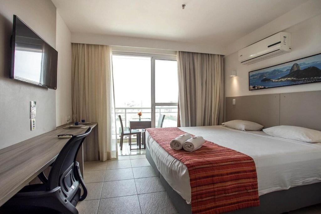 a hotel room with a bed and a desk and a window at Flat 804 - Conforto, praticidade e vista panorâmica em Macaé in Macaé