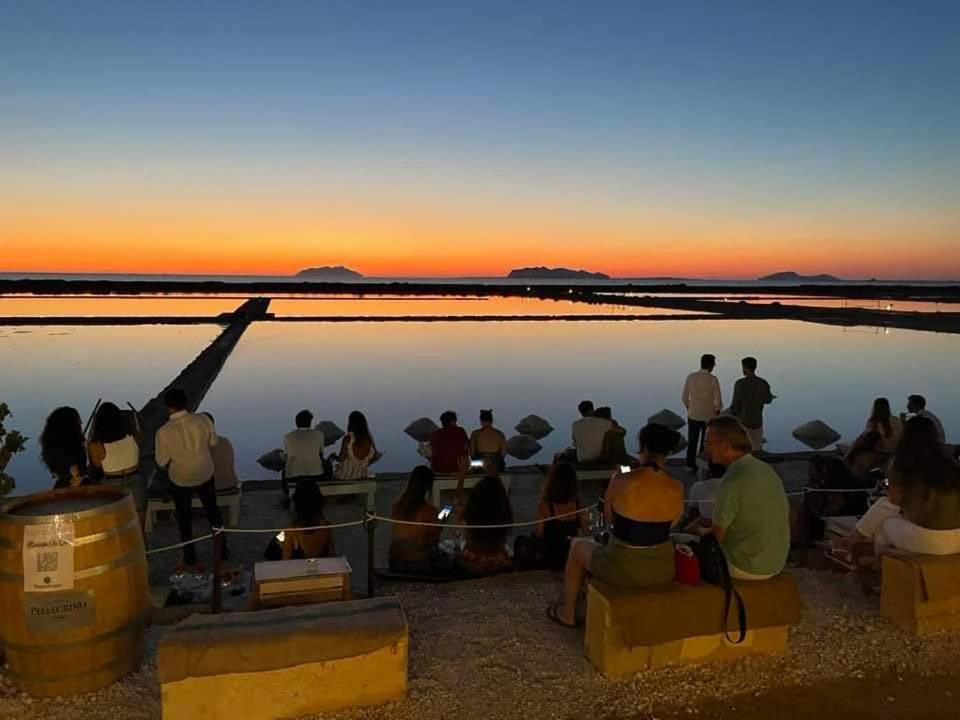 grupa ludzi siedzących na plaży obserwujących zachód słońca w obiekcie Appartamento Mattia w mieście Marsala