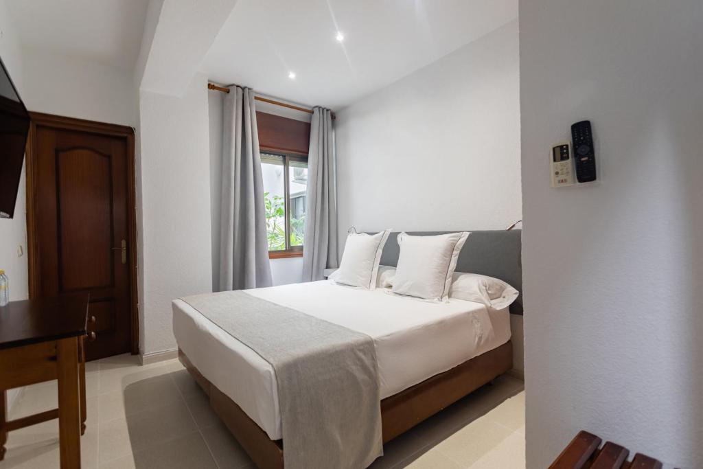 a bedroom with a bed with white sheets and a window at Hostal La Costa in El Ejido