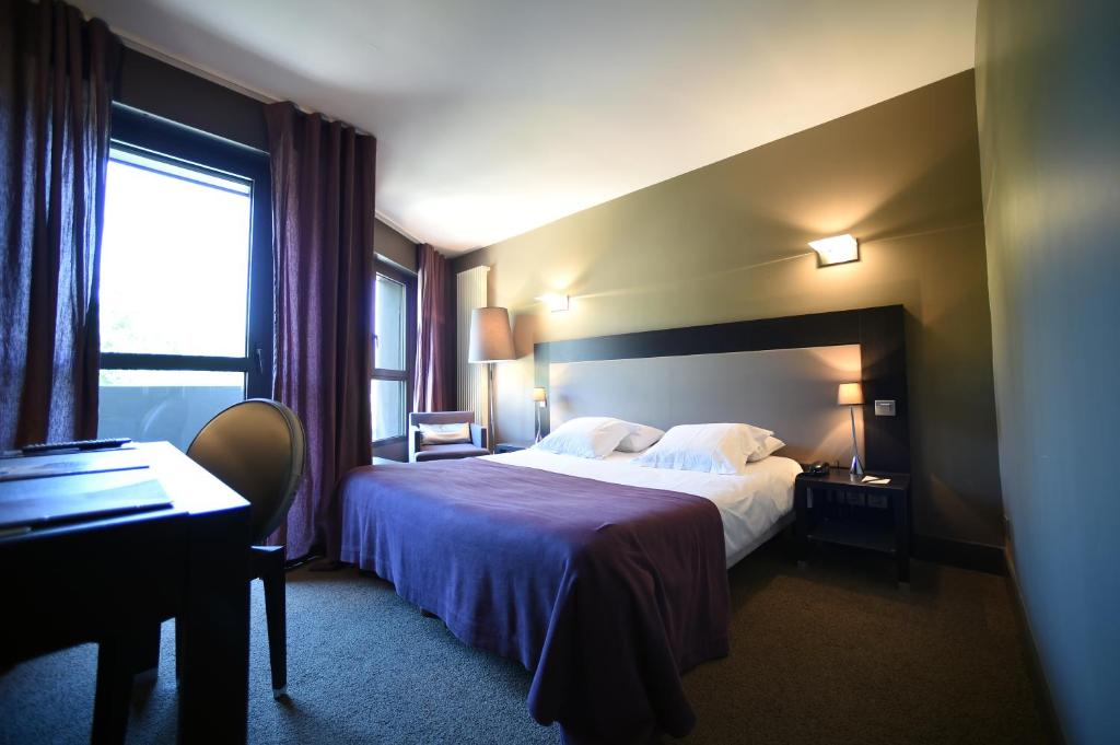 a hotel room with a bed and a desk and a window at Hôtel Les Rives in Guebwiller