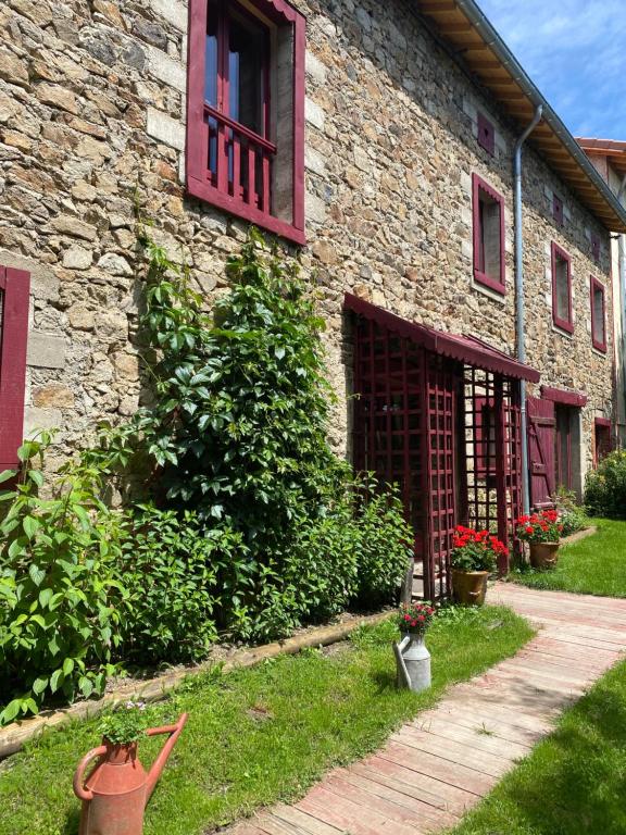 ein Steingebäude mit roten Fenstern und Pflanzen im Hof in der Unterkunft La Forge in Allègre