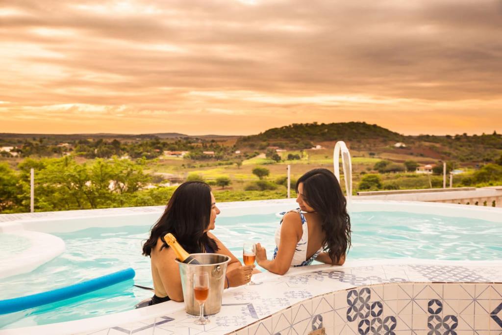 two women sitting in a swimming pool with drinks at Flor de Mandacaru Pousada in Boqueirão (1)