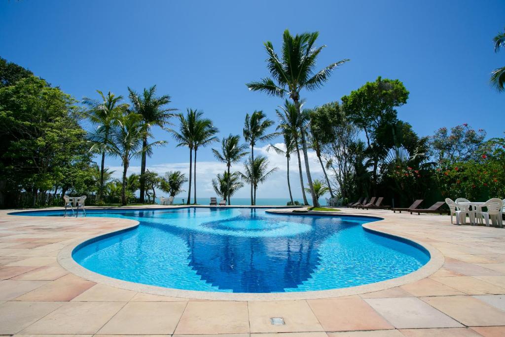 a swimming pool with palm trees and the ocean at Pousada Vila do Beco in Arraial d'Ajuda