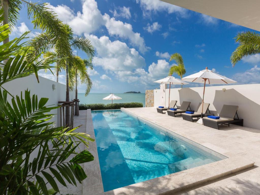 a pool with chairs and umbrellas next to the ocean at Skye Beach Hotel - Koh Samui in Choeng Mon Beach