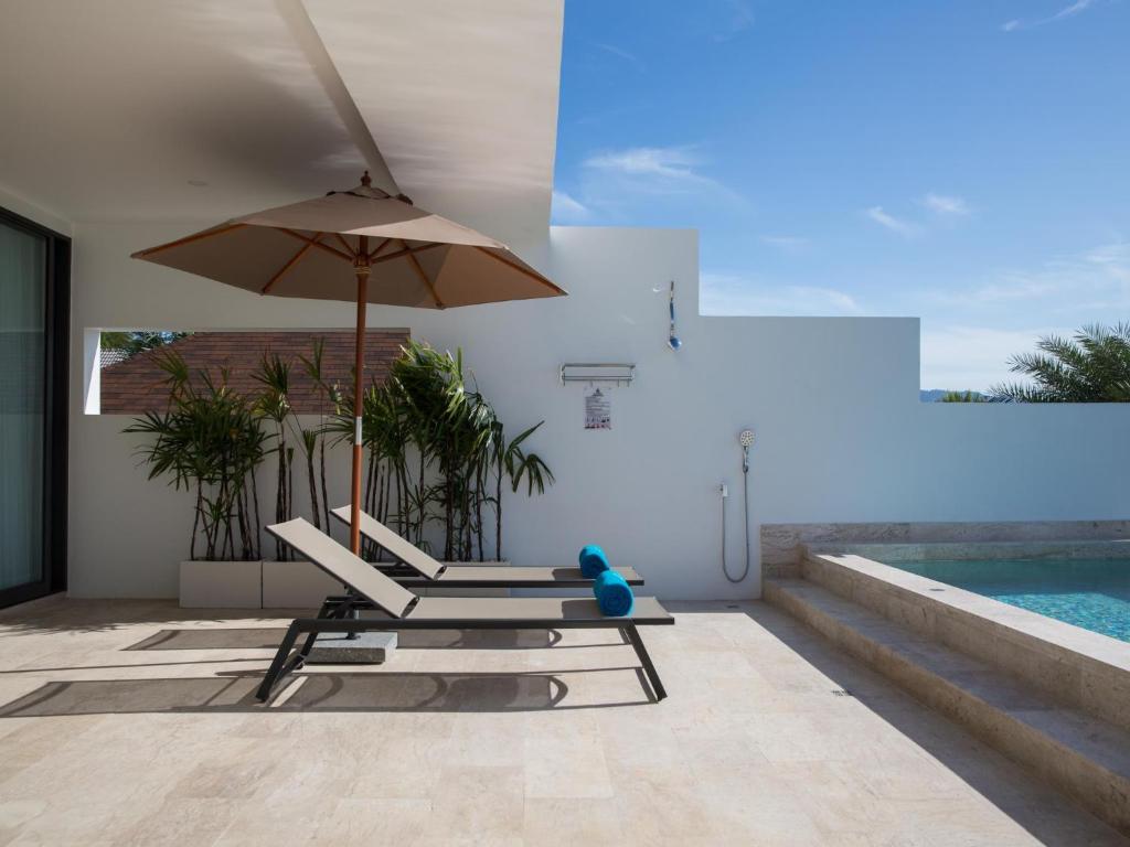 a pair of chairs and an umbrella next to a pool at Skye Beach Hotel - Koh Samui in Choeng Mon Beach