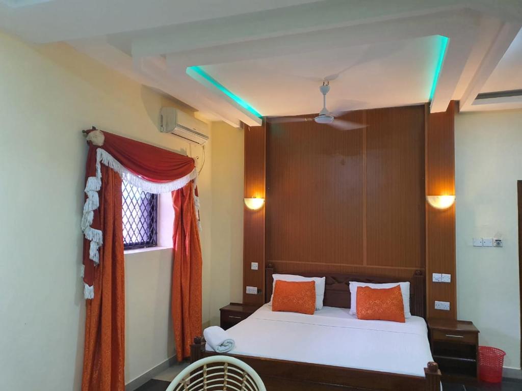 Regency Park Hotel في مومباسا: غرفة نوم مع سرير مع وسائد برتقالية ونافذة