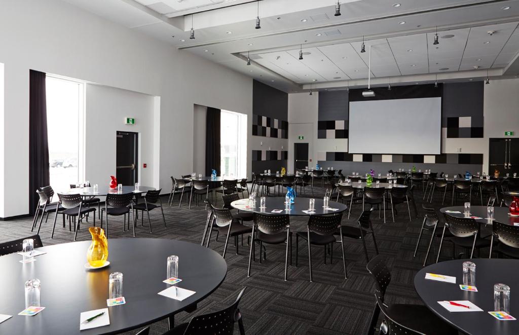 a large room with tables and chairs and a projection screen at Alt Hotel Halifax Airport in Enfield