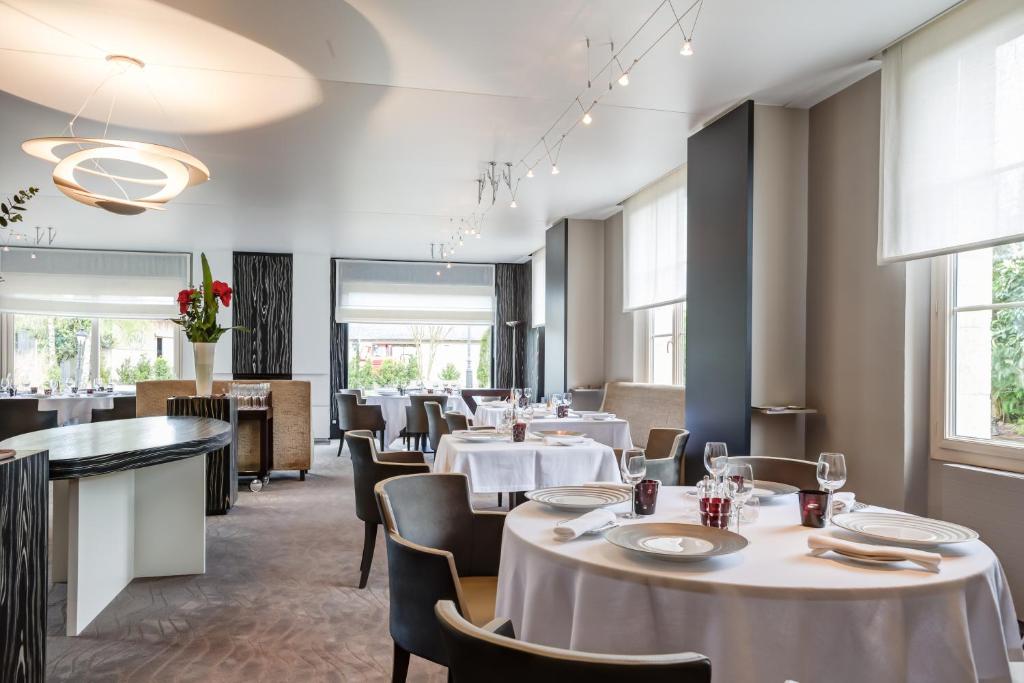 a restaurant with white tables and chairs and windows at Hostellerie de la Renaissance - Teritoria in Argentan