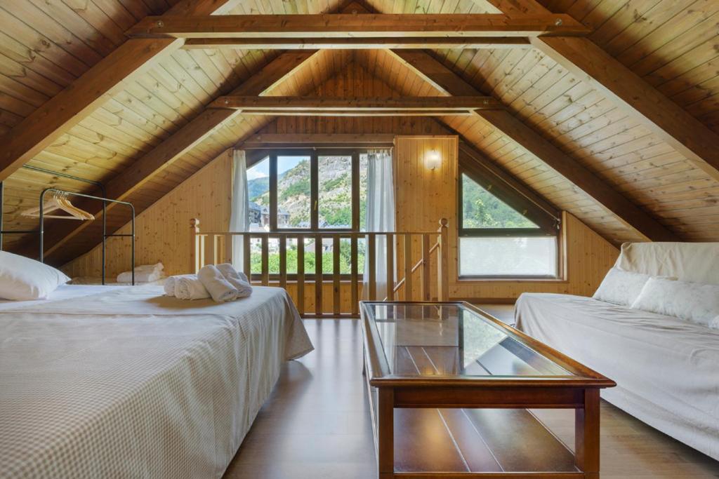 a attic room with two beds and a glass table at Alojamiento Escarrilla Pirineos in Escarrilla