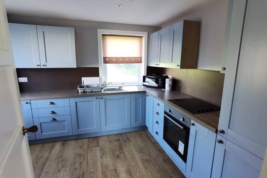 a blue kitchen with white cabinets and a window at Trotternish Avenue Staffin IV51 9JU in Staffin