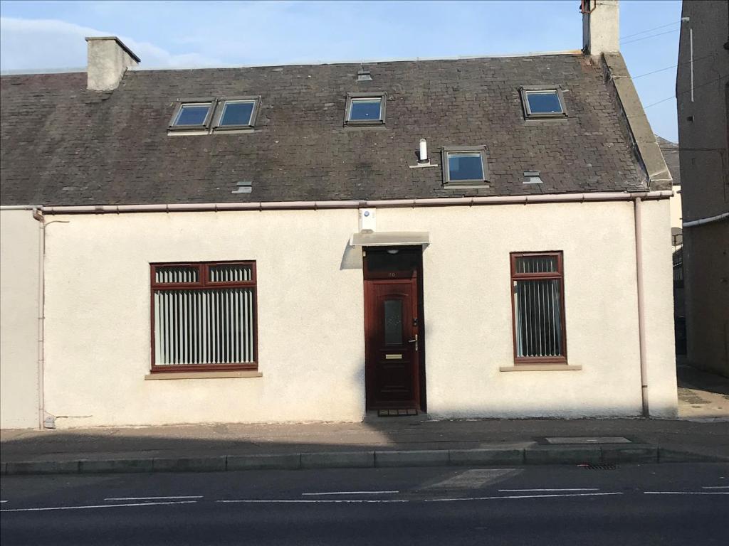 a white building with a red door on a street at 30 College Street, Buckhaven, Leven, Fife, KY81JX in Buckhaven