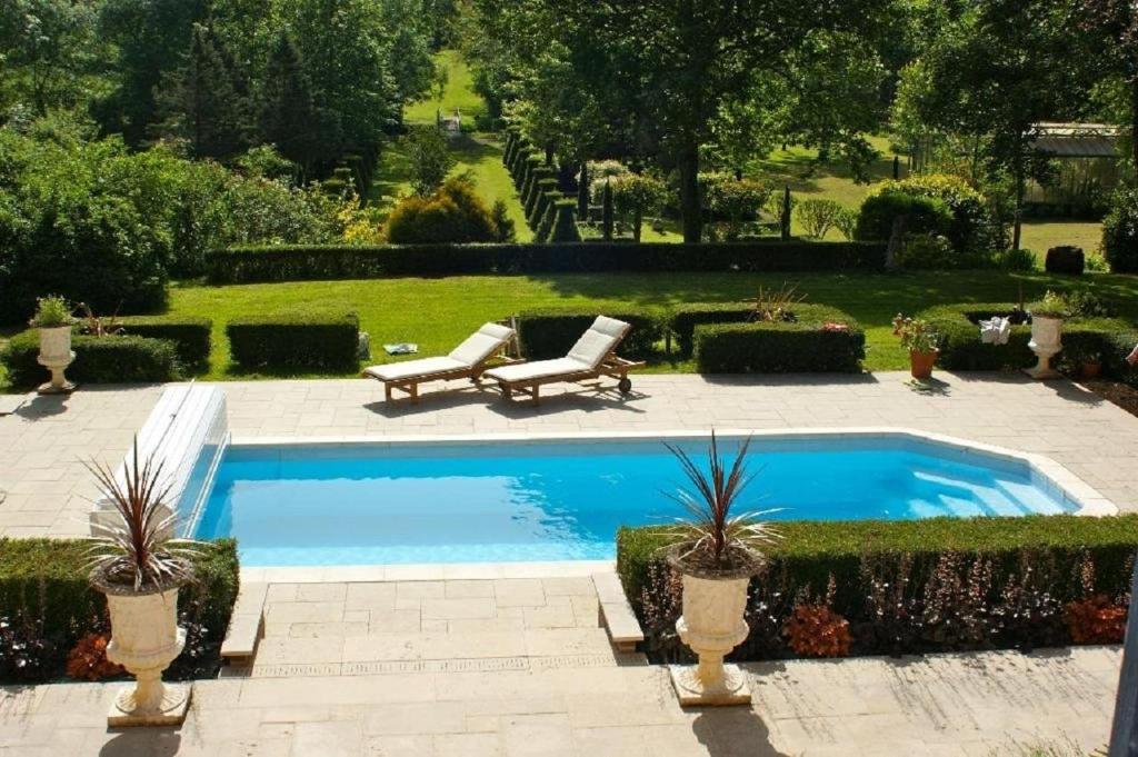 uma piscina num jardim com duas cadeiras e um banco em Le Charme em Mézilles