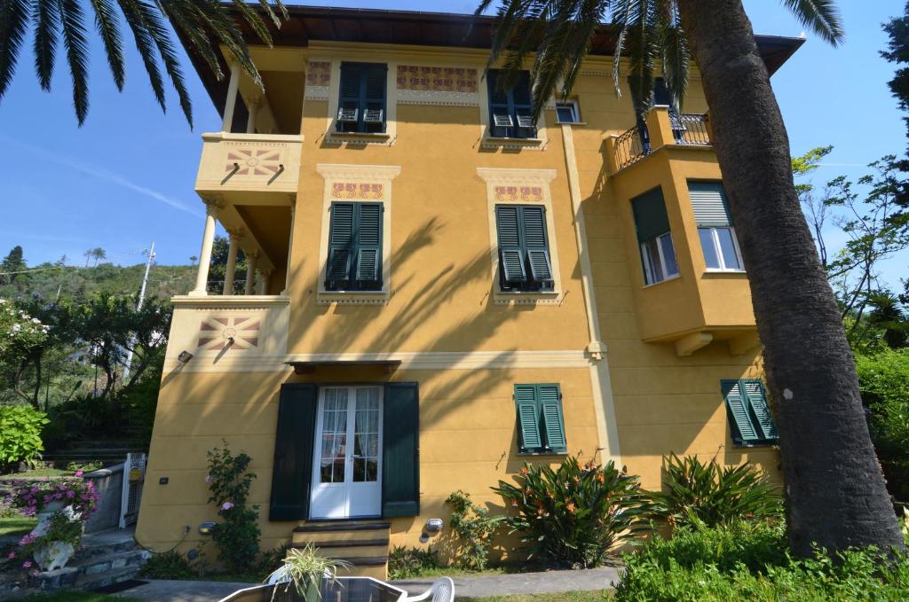 a yellow building with green shutters and a palm tree at Villa Margherita in Levanto