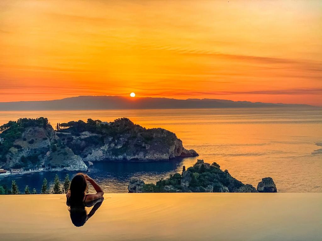 une personne nageant dans l'eau au coucher du soleil dans l'établissement Isola Bella Infinity Suites, à Taormine