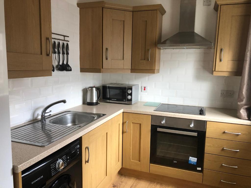 cocina con armarios de madera, fregadero y microondas en Central Lisburn Duplex Apartment Siren Stays, en Lisburn