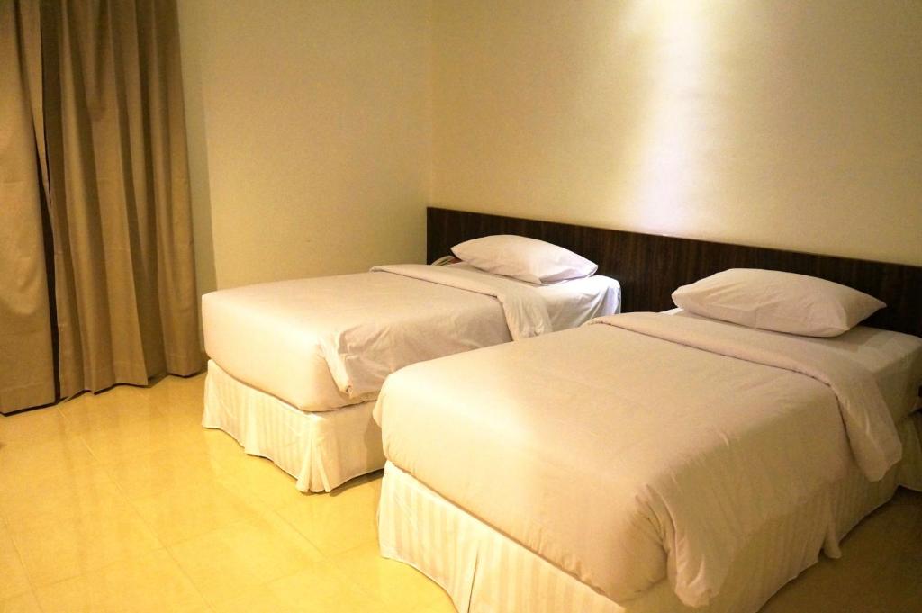 two beds in a hotel room with white sheets at Ameera Hotel in Pekanbaru