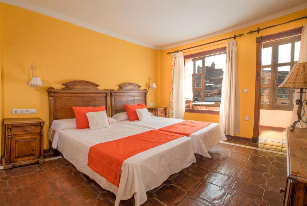 Schlafzimmer mit einem großen Bett mit orangefarbener und weißer Bettwäsche in der Unterkunft Hospederia del Zenete in La Calahorra
