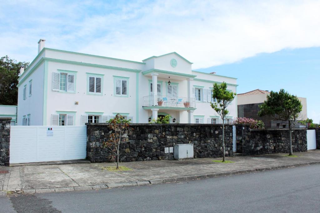 a large white house with a stone wall at Bella Italia Pópulo Guest House in Ponta Delgada