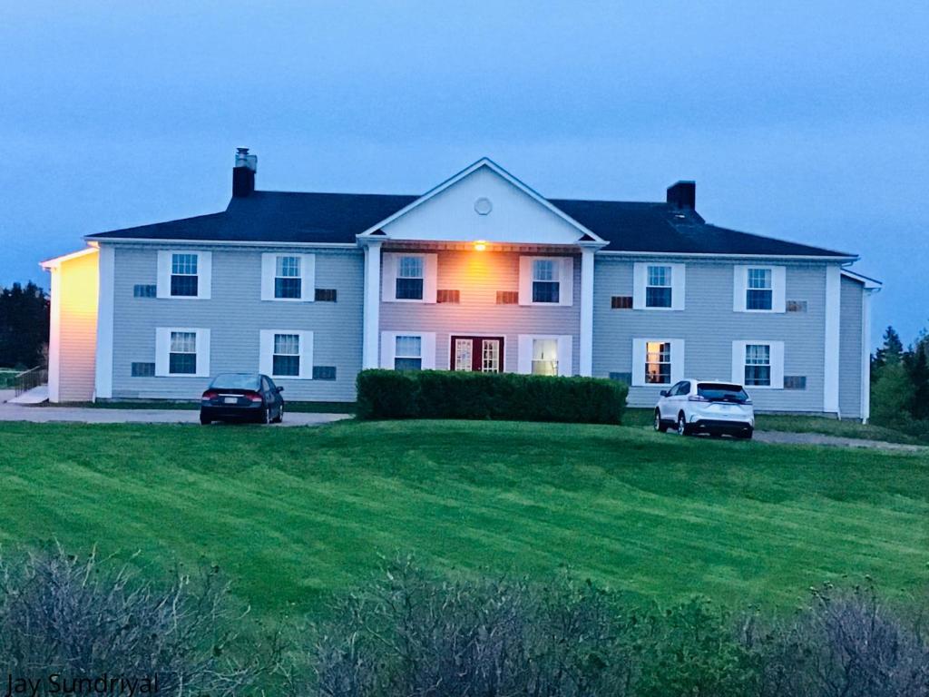 une grande maison blanche avec deux voitures garées dans une cour dans l'établissement Rollo Bay Inn, à Souris