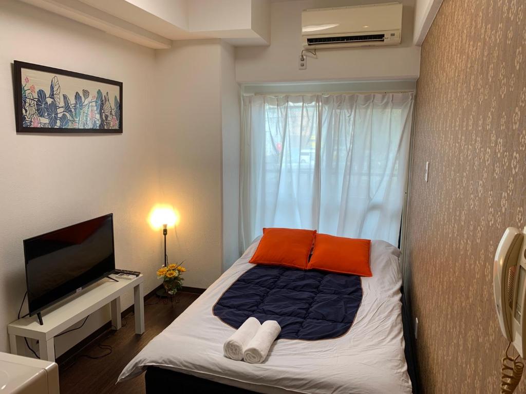 1 dormitorio con 1 cama con almohadas de color naranja y TV en Exsaison Shirokita 201, en Osaka