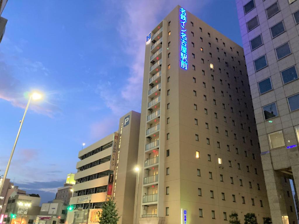 a tall building with a blue neon sign on it at Meitetsu Inn Nagoya Ekimae in Nagoya