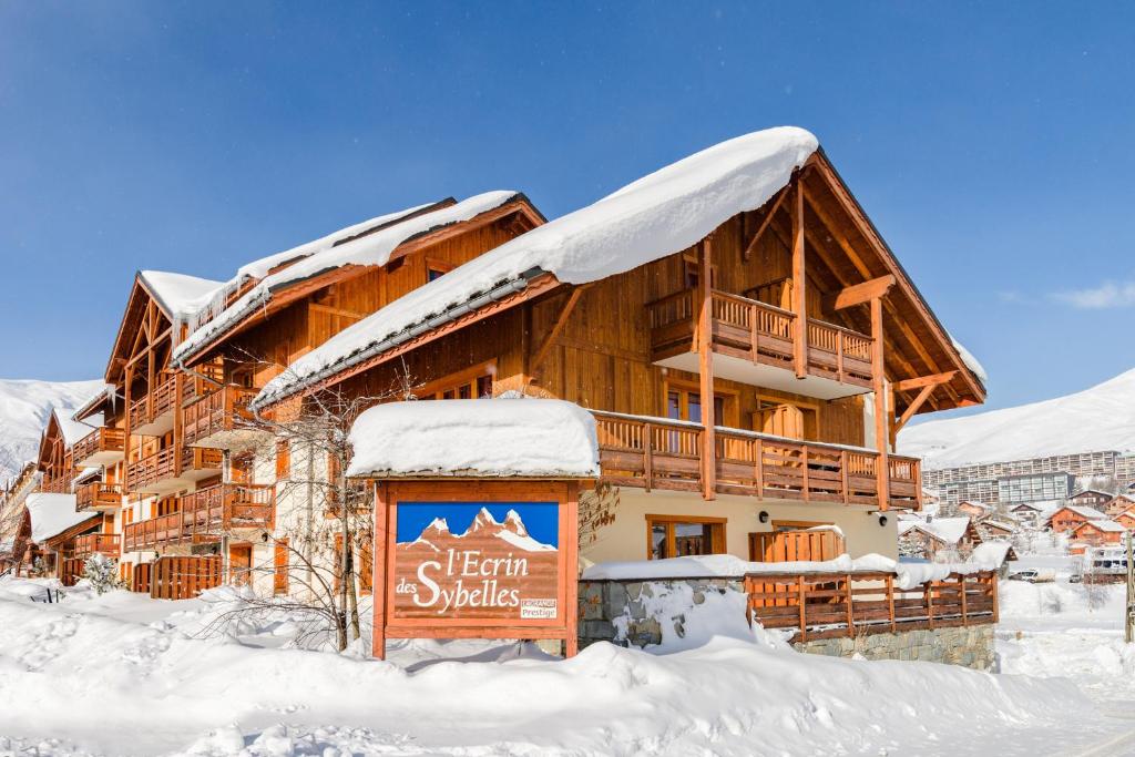 a log cabin in the snow with a sign in front at travelski home select - Résidence L'Ecrin des Sybelles in La Toussuire