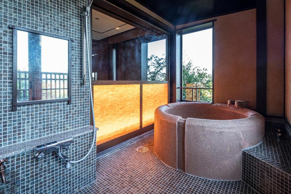 une salle de bain avec une grande baignoire dans une pièce avec des fenêtres dans l'établissement Hakone Kyuan, à Hakone