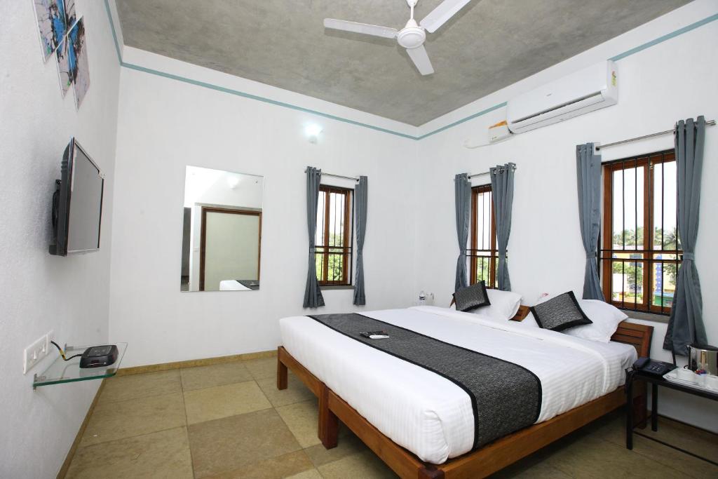 a bedroom with a large white bed and windows at Hotel Du Palais - Auroville Beach in Puducherry