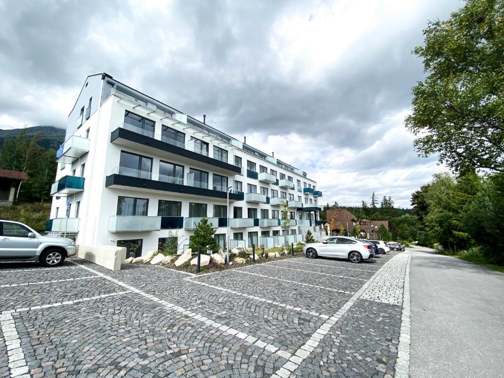 a white building with cars parked in a parking lot at Apartment PEAK - Apartmany Bernard Stary Smokovec in Nový Smokovec