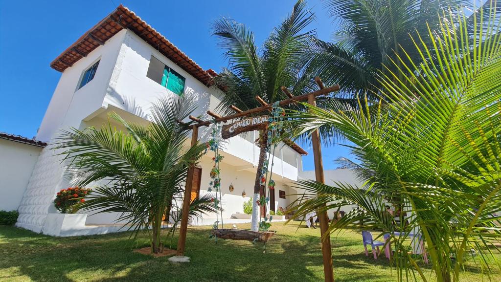 une maison blanche avec des palmiers devant elle dans l'établissement POUSADA CENÁRIO IDEAL, à Icapuí