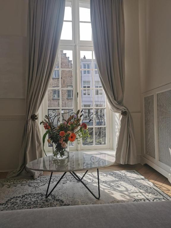 a vase of flowers on a glass table in front of a window at Molenmeers Boutique Guesthouses in Bruges