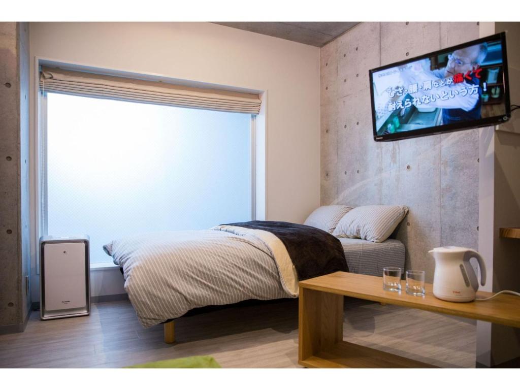 1 dormitorio con 1 cama y TV en la pared en bmj Shinjuku Okubo - Vacation STAY 68278v, en Tokio