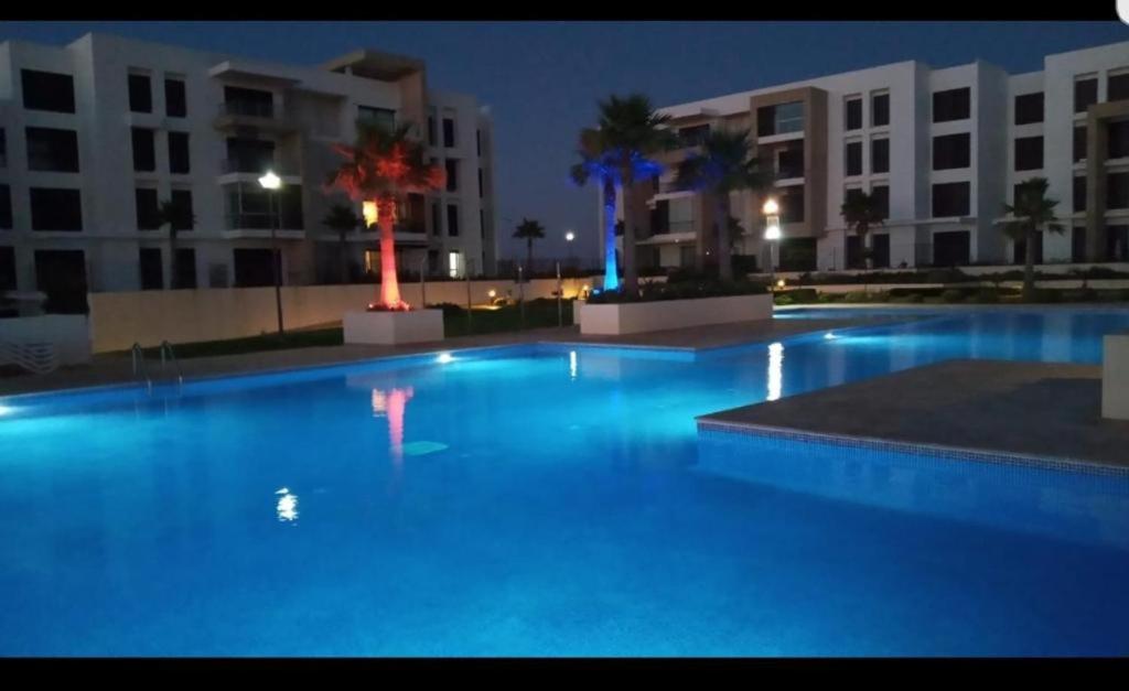Superbe appartement Front de mer Prestigia في Sidi Bouqnadel: مسبح كبير بالليل بالمباني