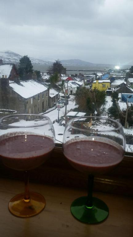 dois copos de vinho em frente a uma janela com uma cidade coberta de neve em Carlingford Mountain and Sea Views em Carlingford