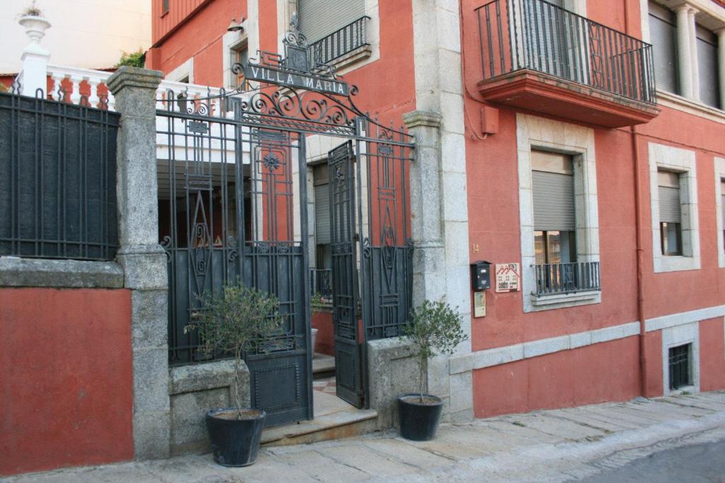 a red building with a black gate and potted plants at Hotel Villa Maria in Fuentes de B&eacute;jar
