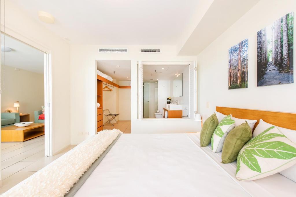 a white bedroom with a large bed and a living room at Lanai Riverside Apartments in Mackay
