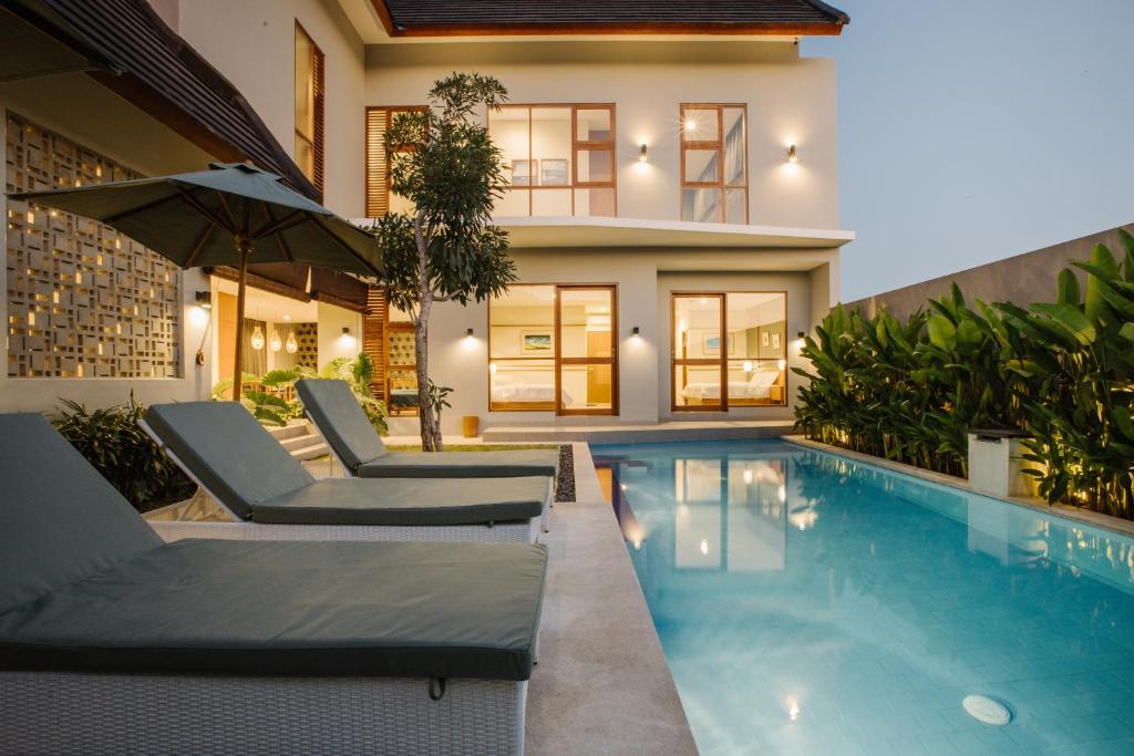 a house with a swimming pool with chairs and an umbrella at Vasudha Hostel Canggu in Canggu