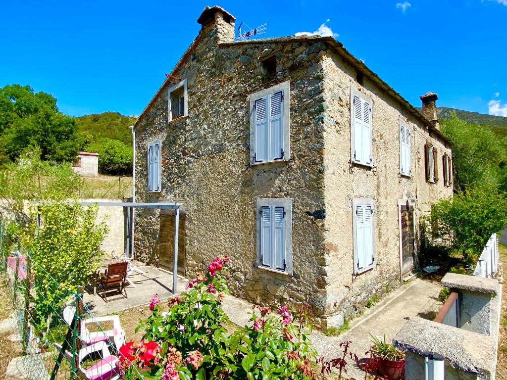 une ancienne maison en pierre avec des fleurs devant elle dans l'établissement Casa Orani, à Ponte-Leccia