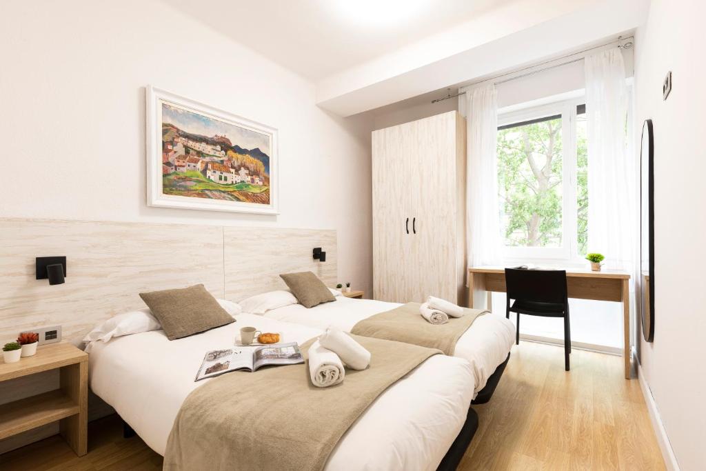 two beds in a hotel room with a desk and a desk at AB Eixample Viladomat Apartments in Barcelona